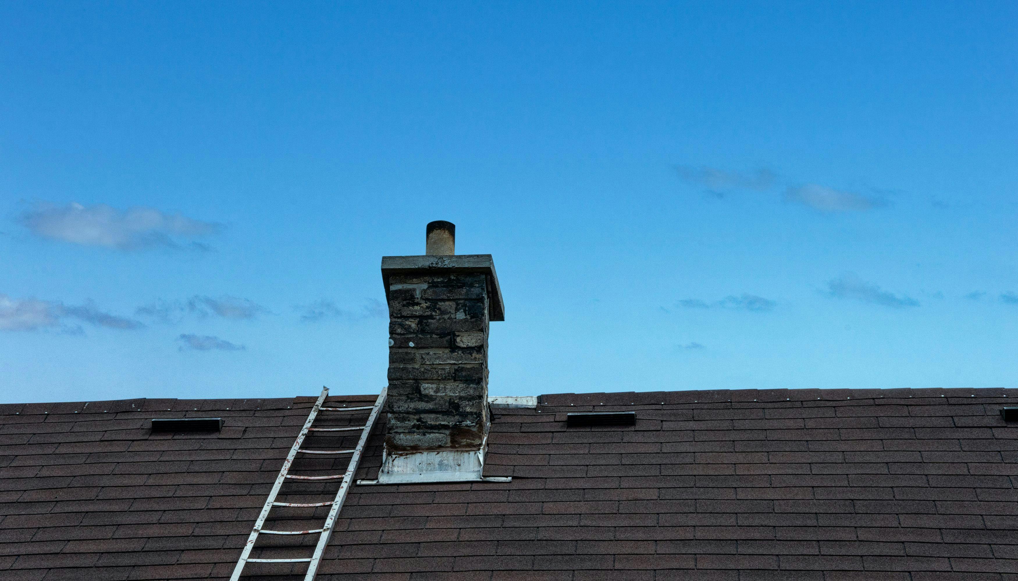 A ladder placed on a roof with a chimney for roof inspection purposes.