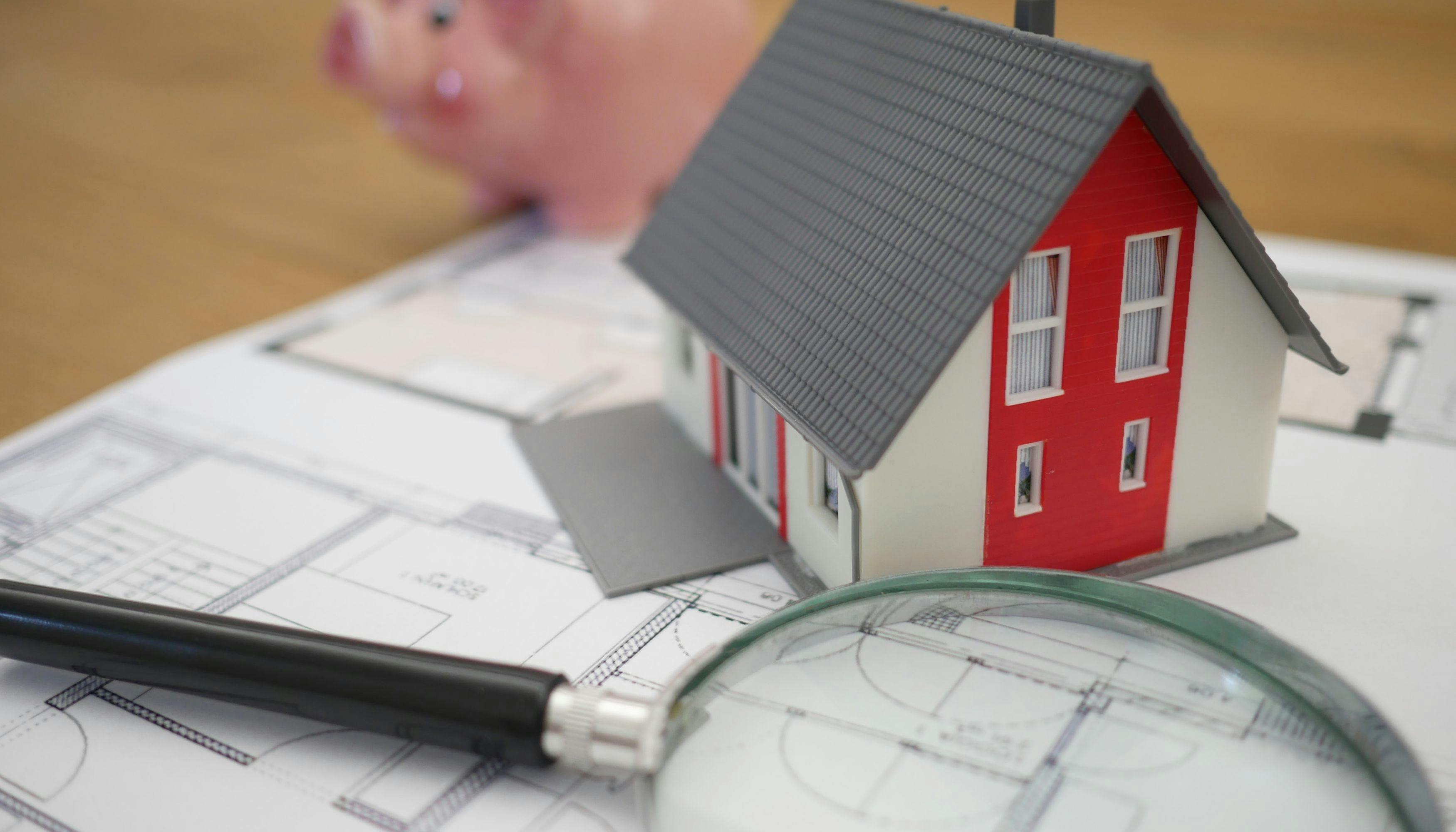 A blueprint featuring a house model, a magnifying glass, and a piggy bank, symbolizing the evaluation of roofing cost.